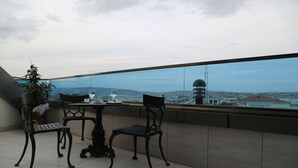 Een balkon met twee stoelen en een tafel, met uitzicht op een stadsgezicht met een toren.