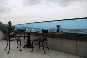 A balcony with two chairs and a table, overlooking a cityscape with a tower.