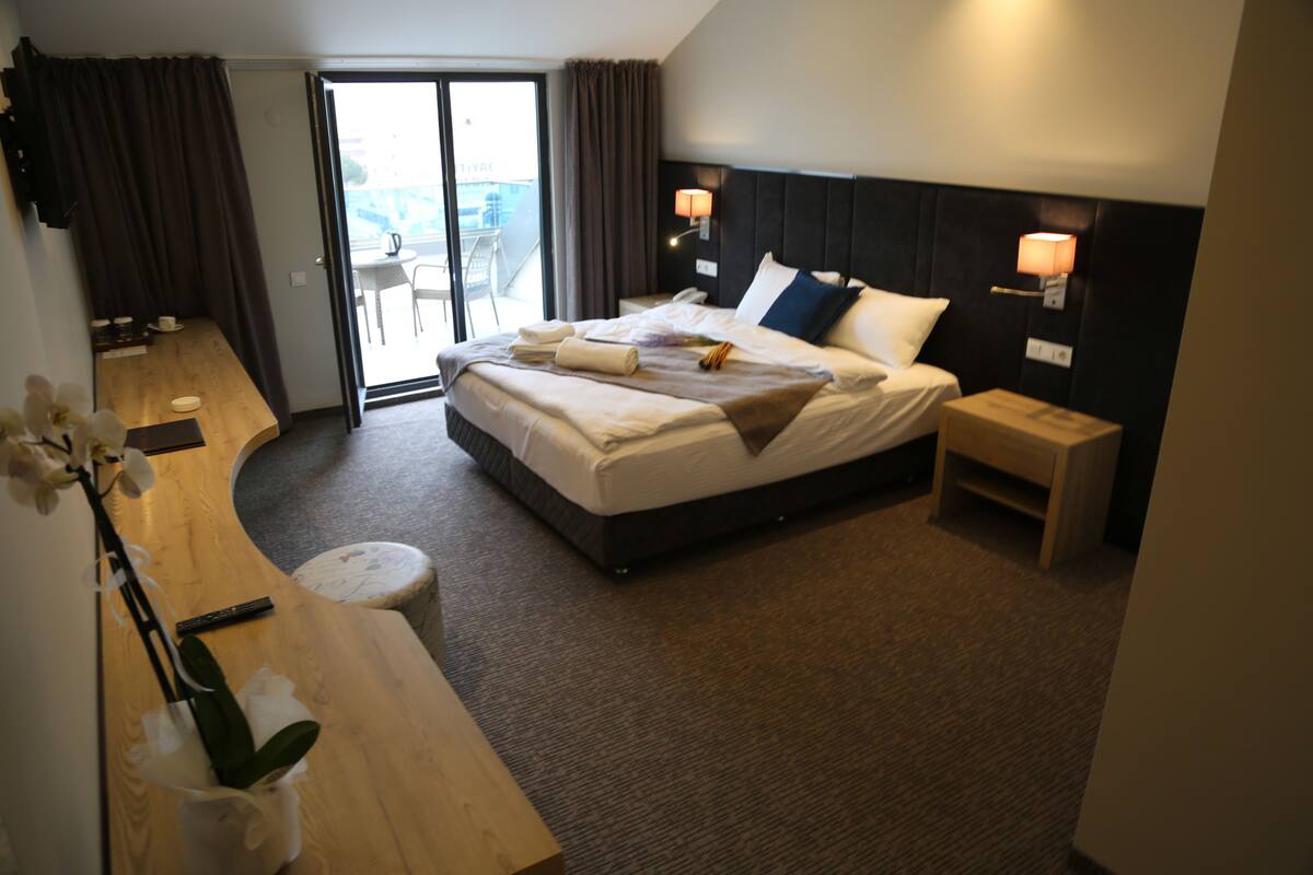 Een moderne hotelkamer met een groot bed, een klein bureau, een stoel, een nachtkastje en uitzicht op het balkon.