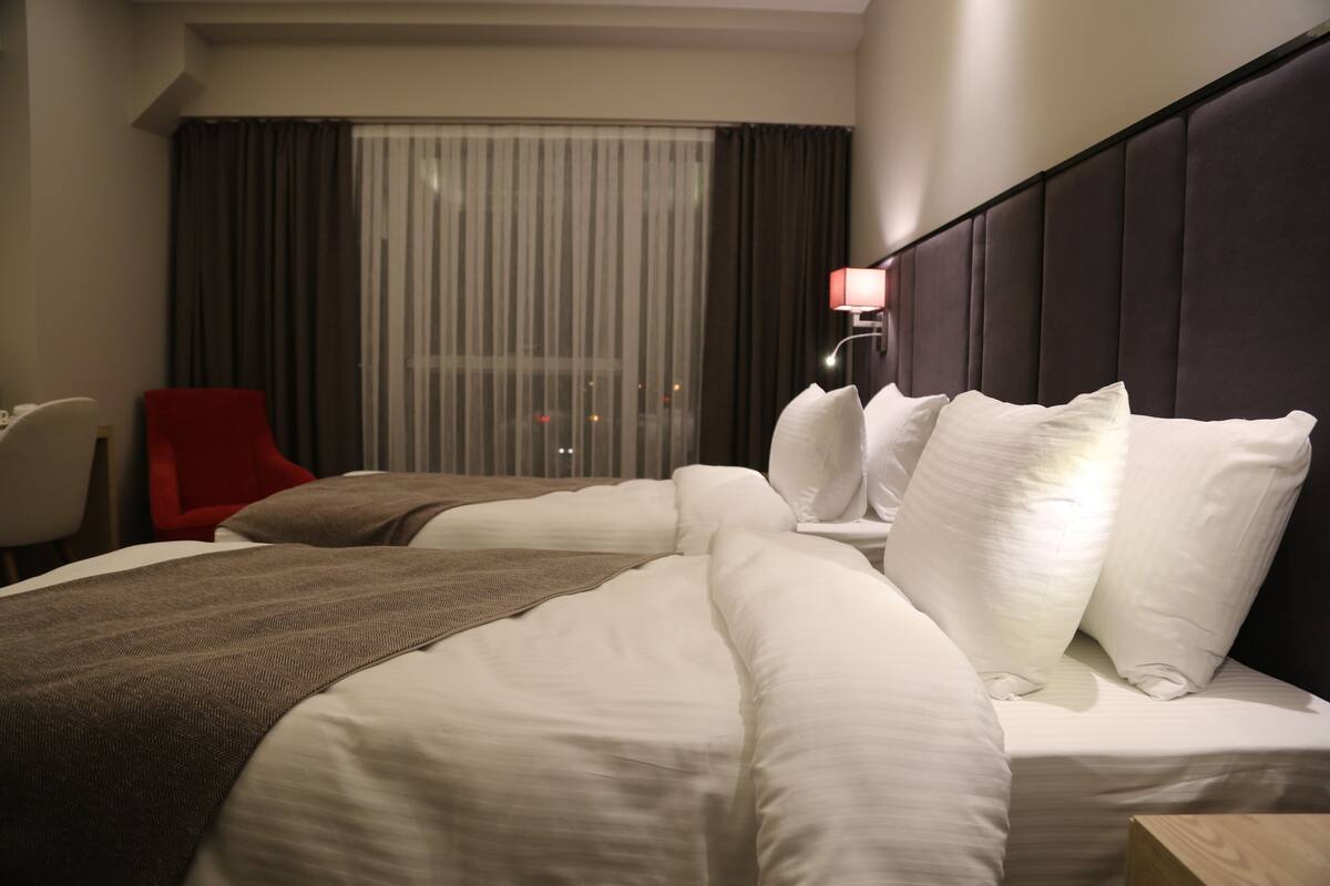 Een hotelkamer met een groot bed, een rode stoel, een raam met gordijnen en een wandlamp.