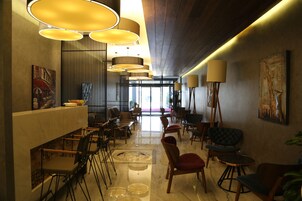A modern interior with a long reception desk, multiple seating areas, and pendant lighting.