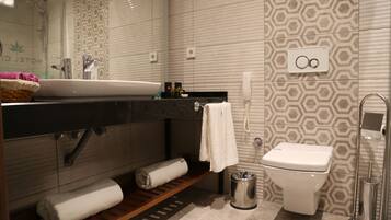 A modern bathroom with a sink, towel rack, toilet, and a trash bin.