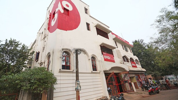 A building with a large red logo on the side, multiple windows, and a red gate. - OYO 4108 near Kalinga Hospital (Bhubaneshwar)