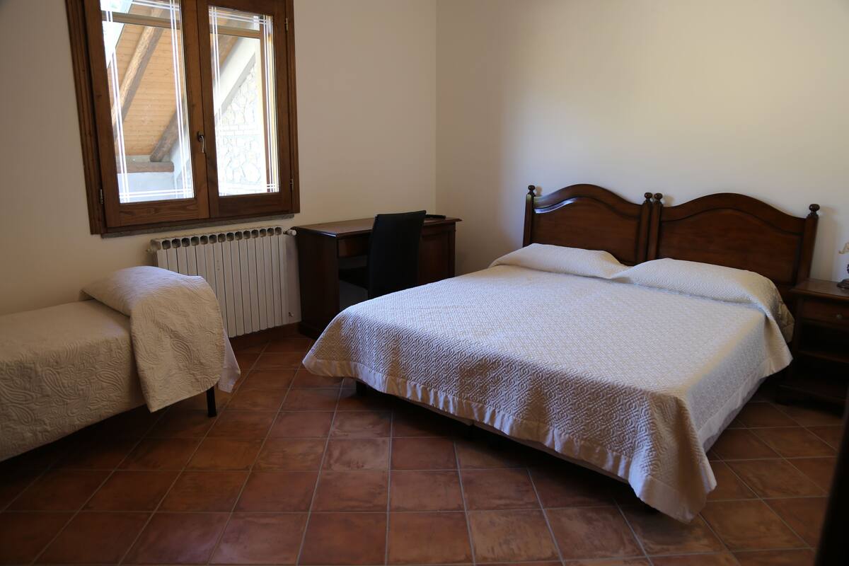 Ein Schlafzimmer mit einem großen Bett, einem kleineren Bett, einem Schreibtisch und einem Stuhl.