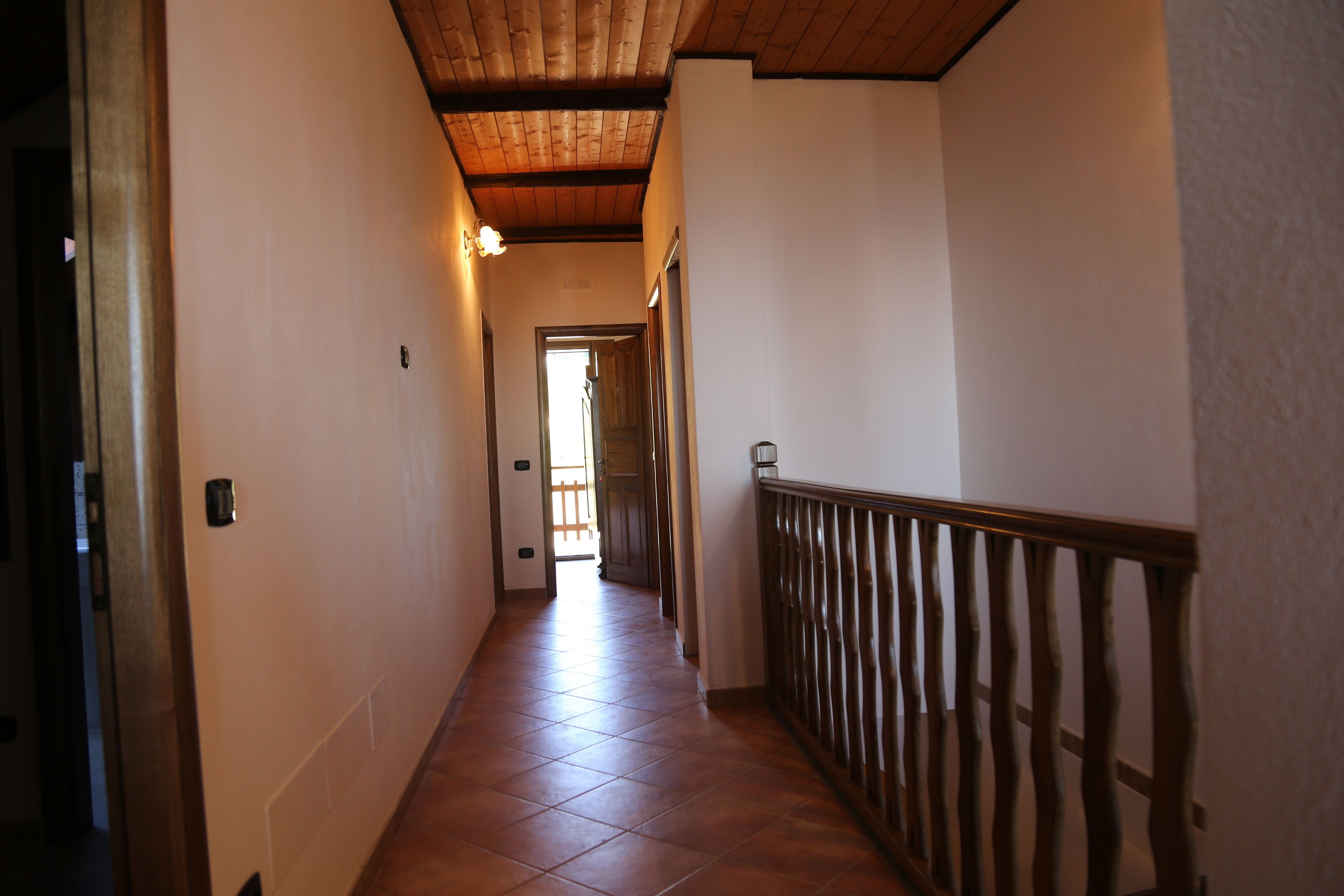 A corridor with a wooden ceiling, tiled floor, and a wooden railing on one side.