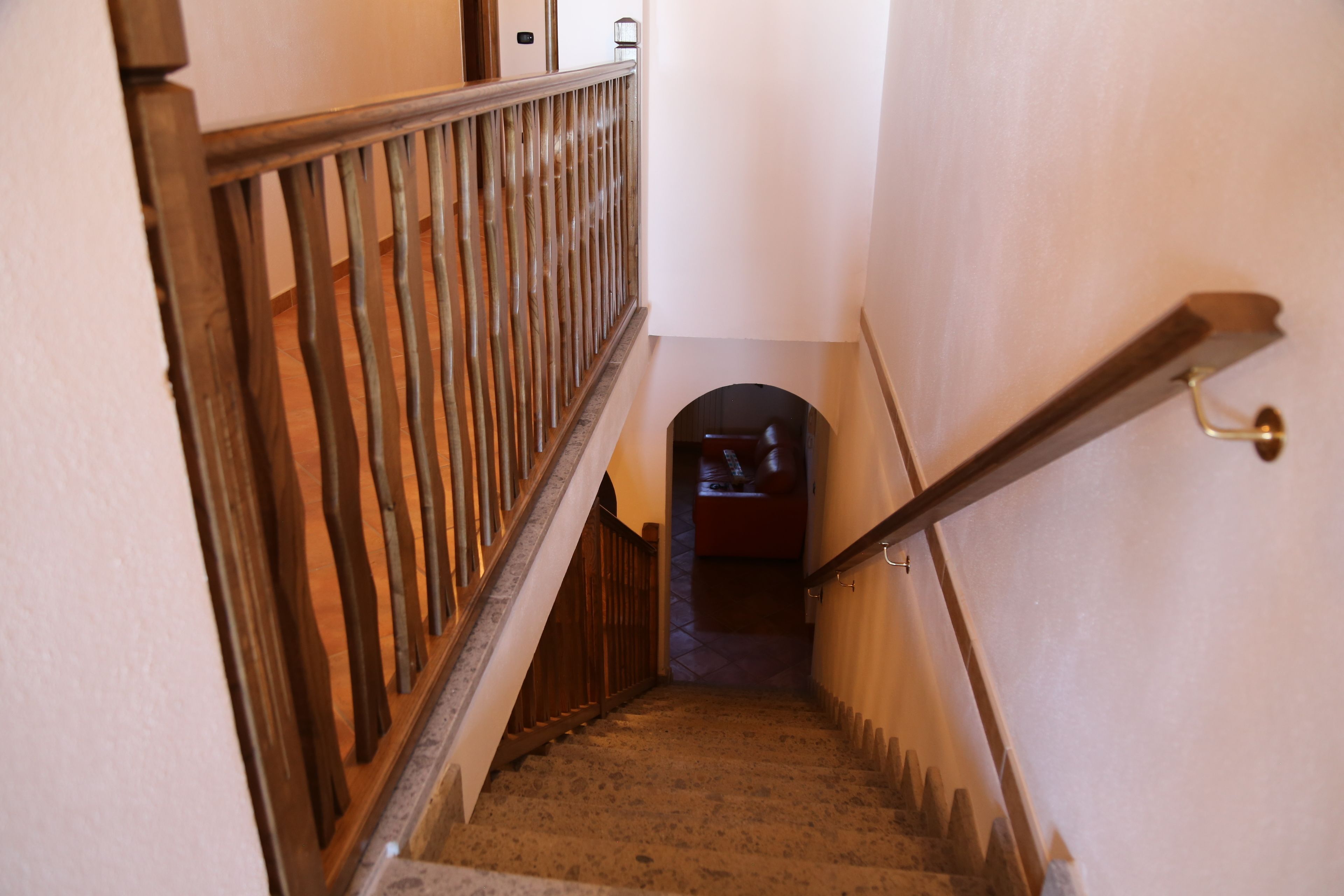 Eine Treppe mit hölzernen Geländern und Handlauf, die zu einem rundbogigen Durchgang führt.