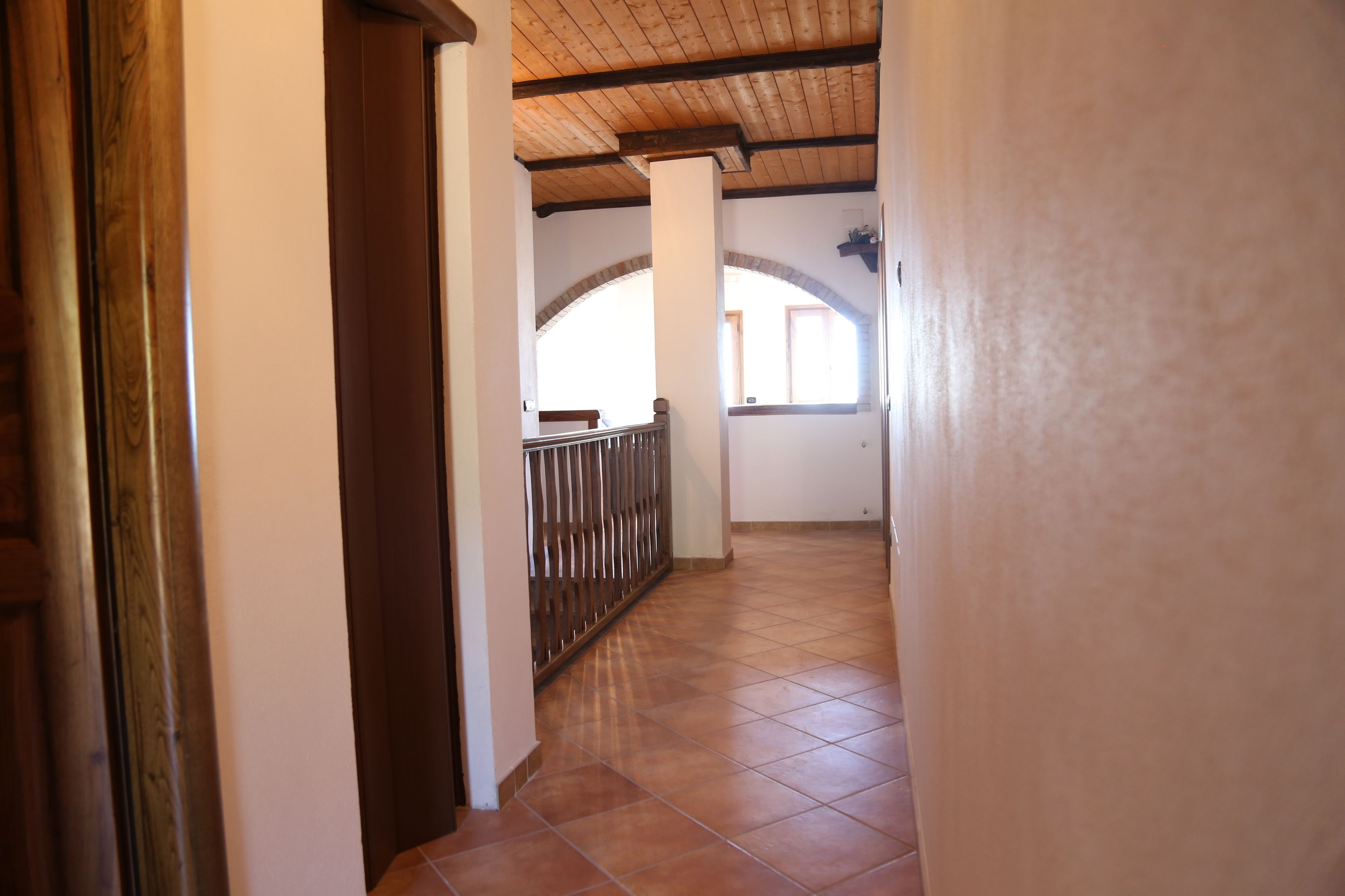 A corridor with tiled flooring, wooden beams on the ceiling, and a metal railing.