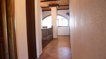 A corridor with tiled flooring, wooden beams on the ceiling, and a metal railing.