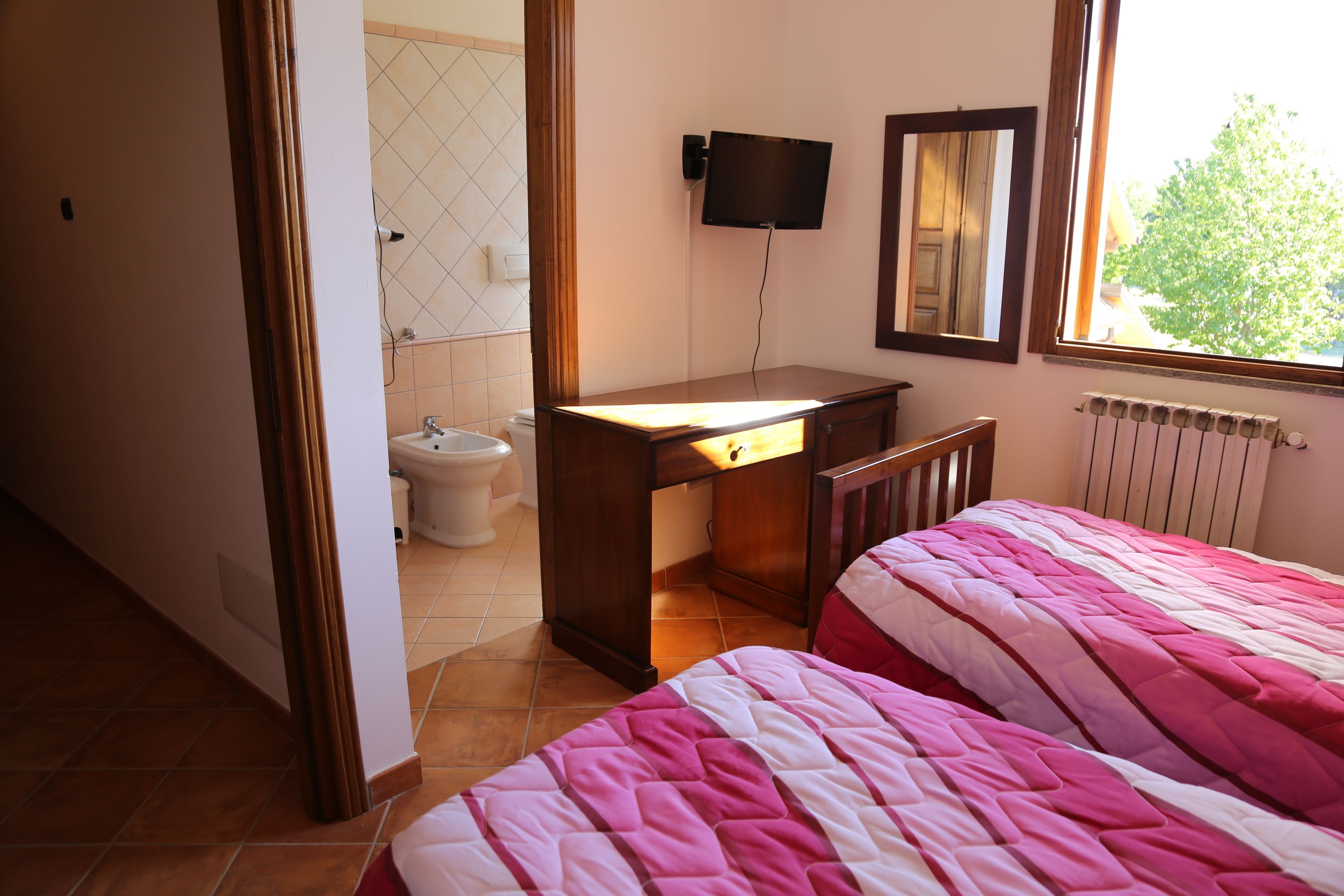 Un dormitorio con cama, escritorio, silla, televisión y ventana.