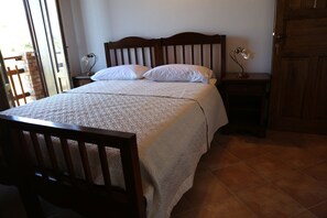 A bedroom with a wooden bed, white bedding, a nightstand with a lamp, and a door. - Agriturismo Pirara (Gerocarne)