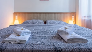 A double bed with a floral-patterned bedspread, two folded towels, bedside lamps, and a wooden headboard. - Penzion U Vlka (Ceske Budejovice)