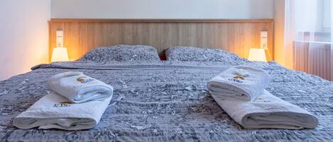 Una cama doble con edredón estampado con motivos florales, dos toallas dobladas, lámparas de noche y un cabecero de madera.