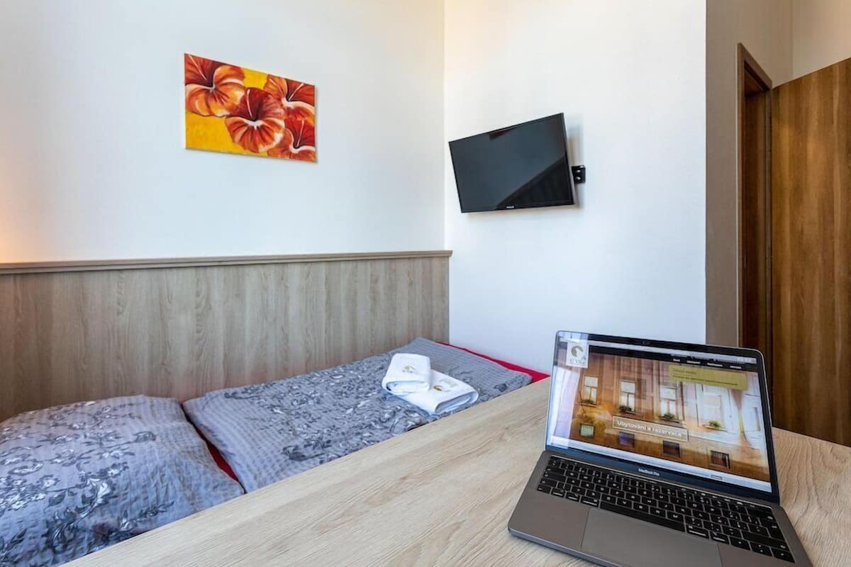 A hotel room with a bed, a laptop, a flat-screen TV, and a painting on the wall.
