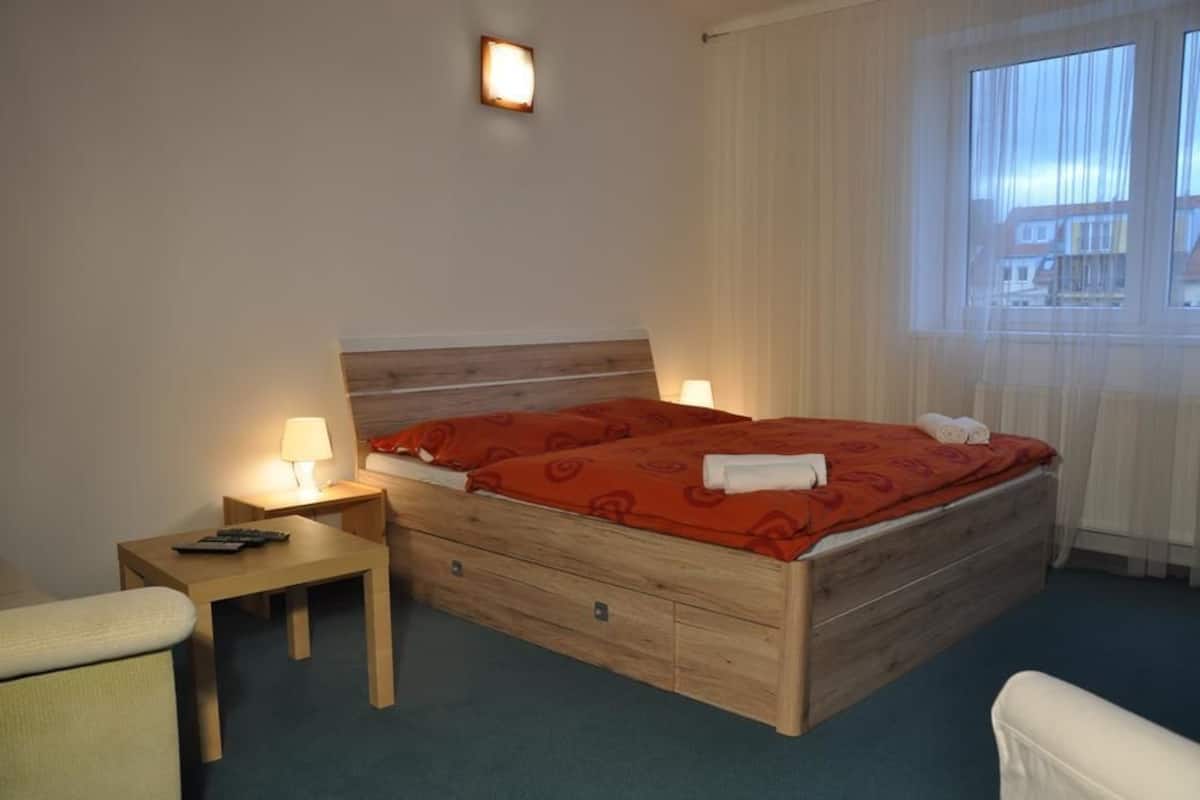 A hotel room with a wooden bed, two bedside tables with lamps, a chair, and a window with curtains.