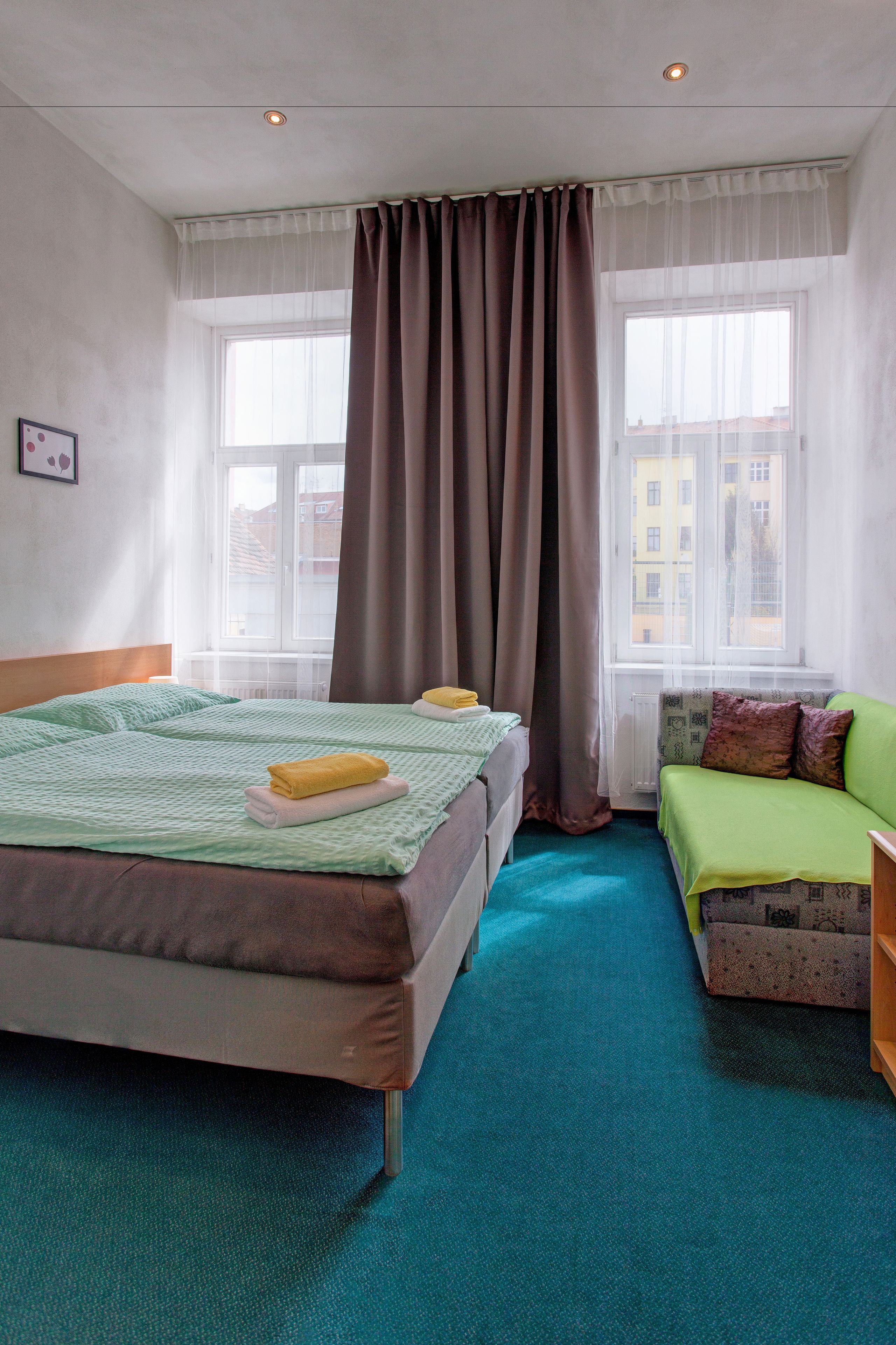 Habitación de hotel con cama, sofá, ventana con cortinas y vista a edificios.