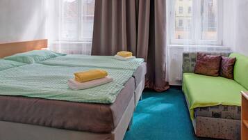 Habitación de hotel con cama, sofá, ventana con cortinas y vista a edificios.