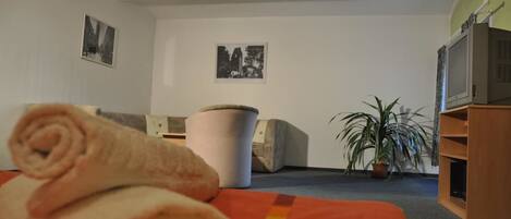 A hotel room with a bed, a television, a trash bin, and two framed pictures on the wall.
