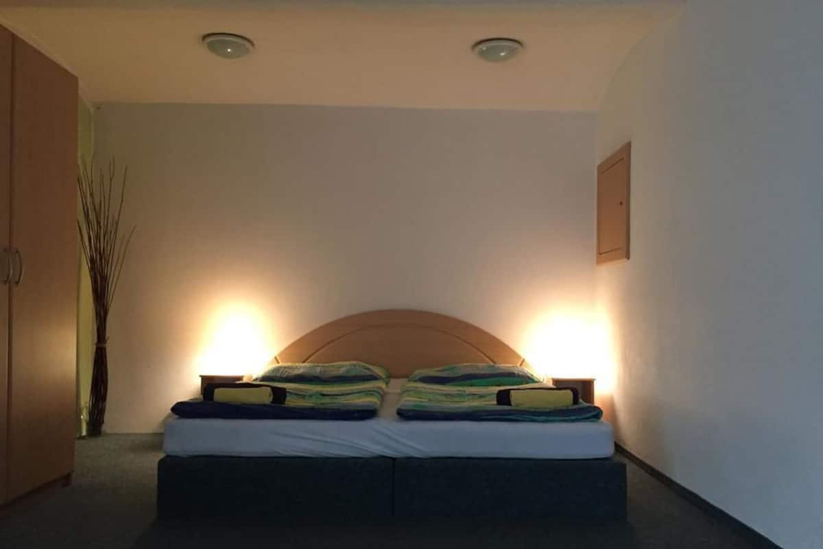 A bedroom with a bed, two bedside lamps, a wooden headboard, and a wall-mounted light fixture.