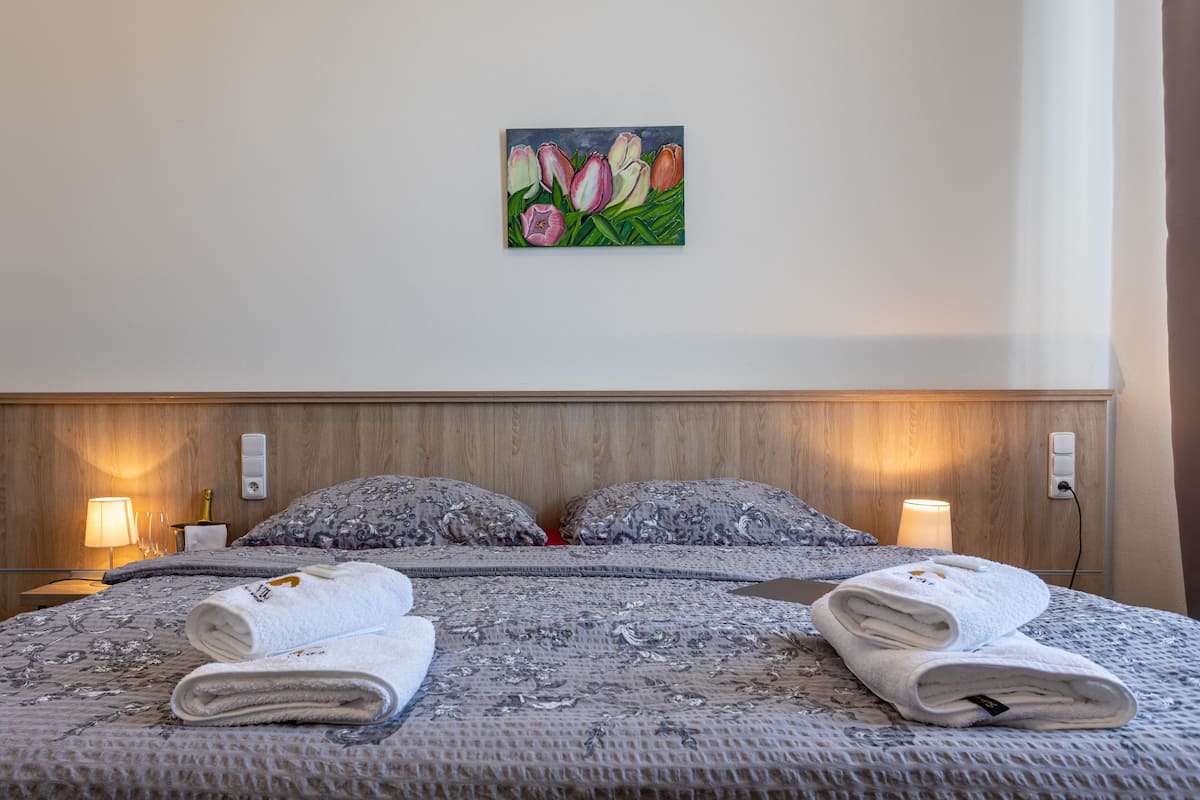 A hotel room with a large bed, two bedside lamps, a painting of tulips on the wall, and a wooden headboard.
