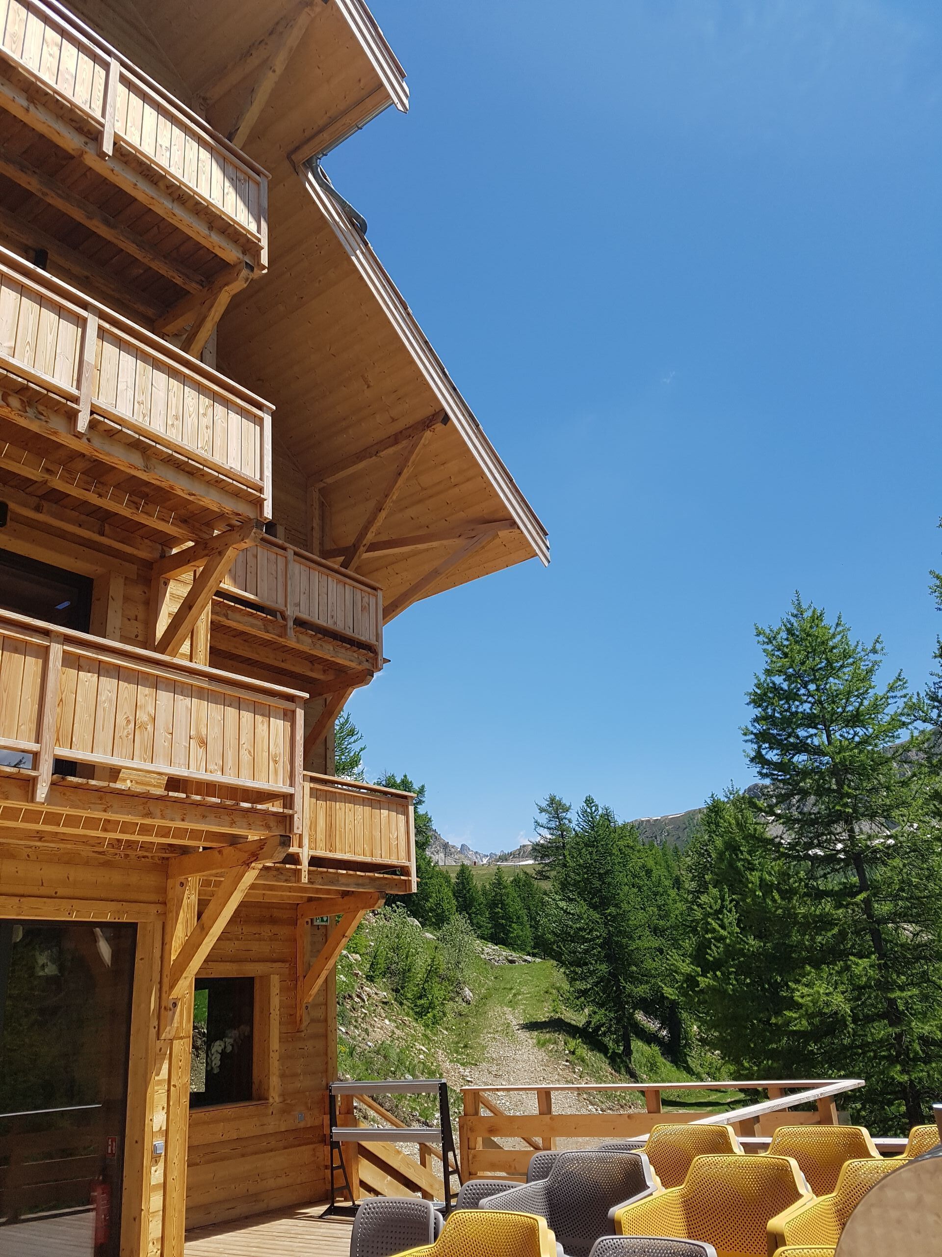 Ein mehrstöckiges Holzgebäude mit Balkonen, Sitzgelegenheiten im Freien und einer Bergkulisse.