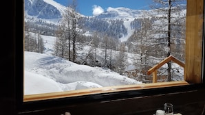Vista per la finestra d'un paisatge de muntanya nevada amb una construcció de cabana de fusta.