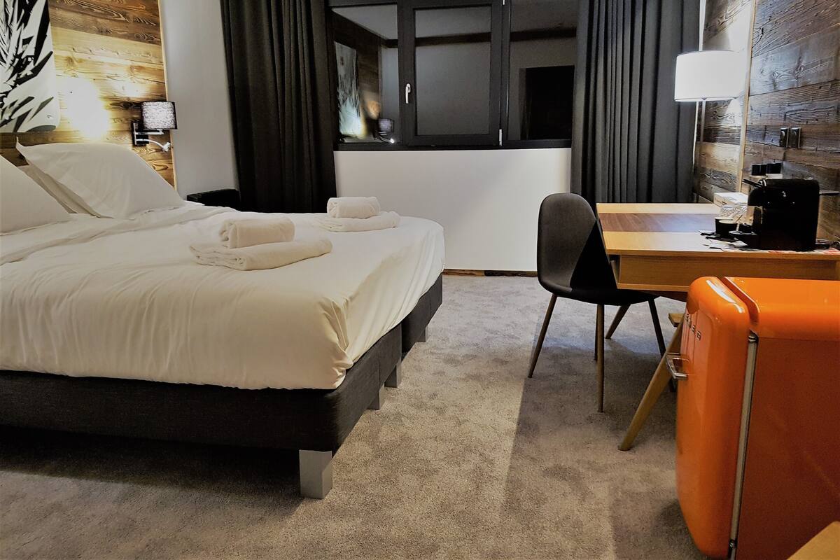 A hotel room with a bed, a desk, a chair, a lamp, and a window with curtains.