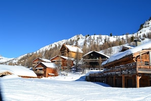 Un pueblo cubierto de nieve con edificios de madera, montañas al fondo y cielos despejados.