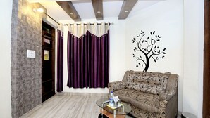 A living room with a patterned sofa, a glass coffee table, a wall-mounted tree decal, a purple curtain, and a tiled floor. - OYO 8278 Supremo (Chandigarh)