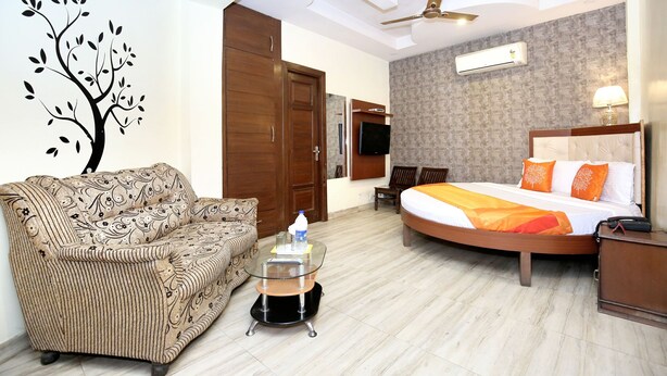 A hotel room with a bed, a sofa, a glass coffee table, a ceiling fan, an air conditioning unit, and a wall-mounted TV. - OYO 8278 Supremo (Chandigarh)