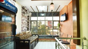 A seating area with a patterned bench, a Pepsi vending machine, and a television on the wall. - OYO 8278 Supremo (Chandigarh)