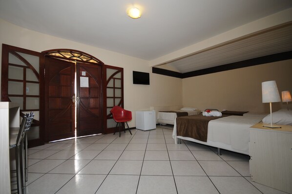 Quarto de hotel com cama, mesa de cabeceira, luminária, cadeira e guarda-roupa com espelho.