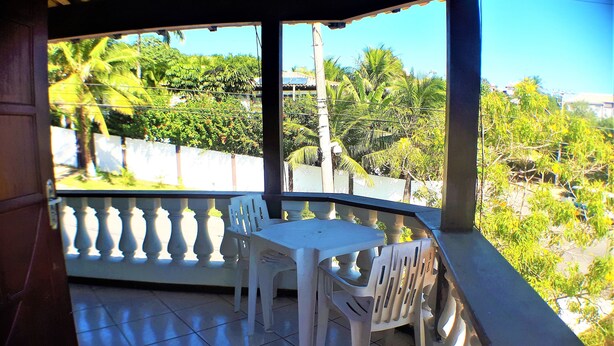 A covered balcony with a white table and chairs, offering a view of greenery and buildings. - Pousada Acquamare (Búzios)