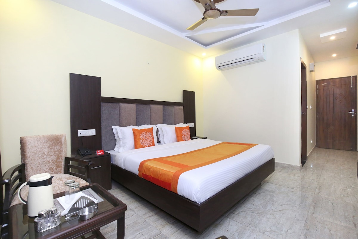 A hotel room with a large bed, a desk with a coffee maker, a chair, and a ceiling fan.