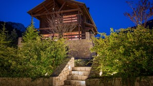 Eine Holzhütte mit einer Steintreppe, die davor hinauf führt, umgeben von Grün.