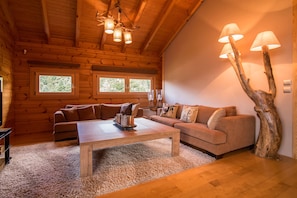 A cozy cabin interior with wooden walls, a sofa, a coffee table, and a unique tree-shaped lamp. - Aelia Hospitality Parnassos (Amfikleia-Elateia)