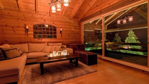 Ein gemütliches Blockhaus-Interieur mit Holzbalkendecke, einem großen Fenster mit Blick auf eine grüne Landschaft, einer Couch und einem Couchtisch mit Kerzen.