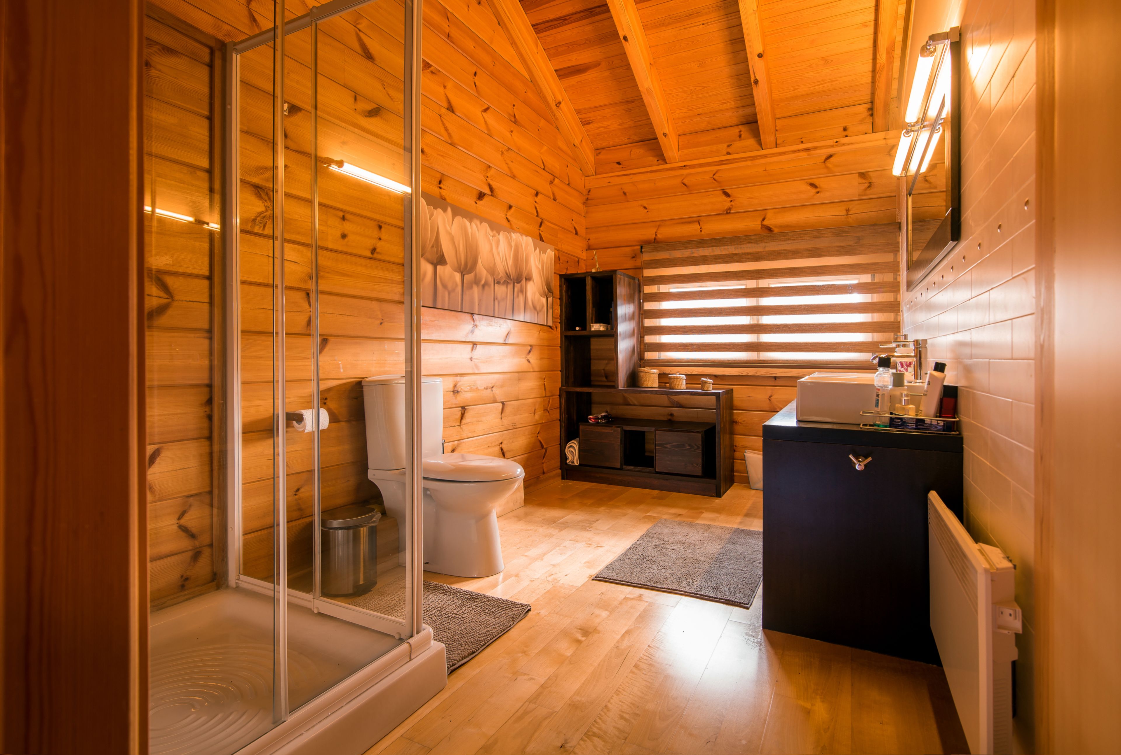A wooden cabin bathroom with a glass shower enclosure, a toilet, a sink, and a built-in cabinet.