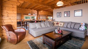 Ein gemütliches Wohnzimmer mit Holzboden, einem grauen Ecksofa, einem braunen Ledersessel und einem Holztisch.