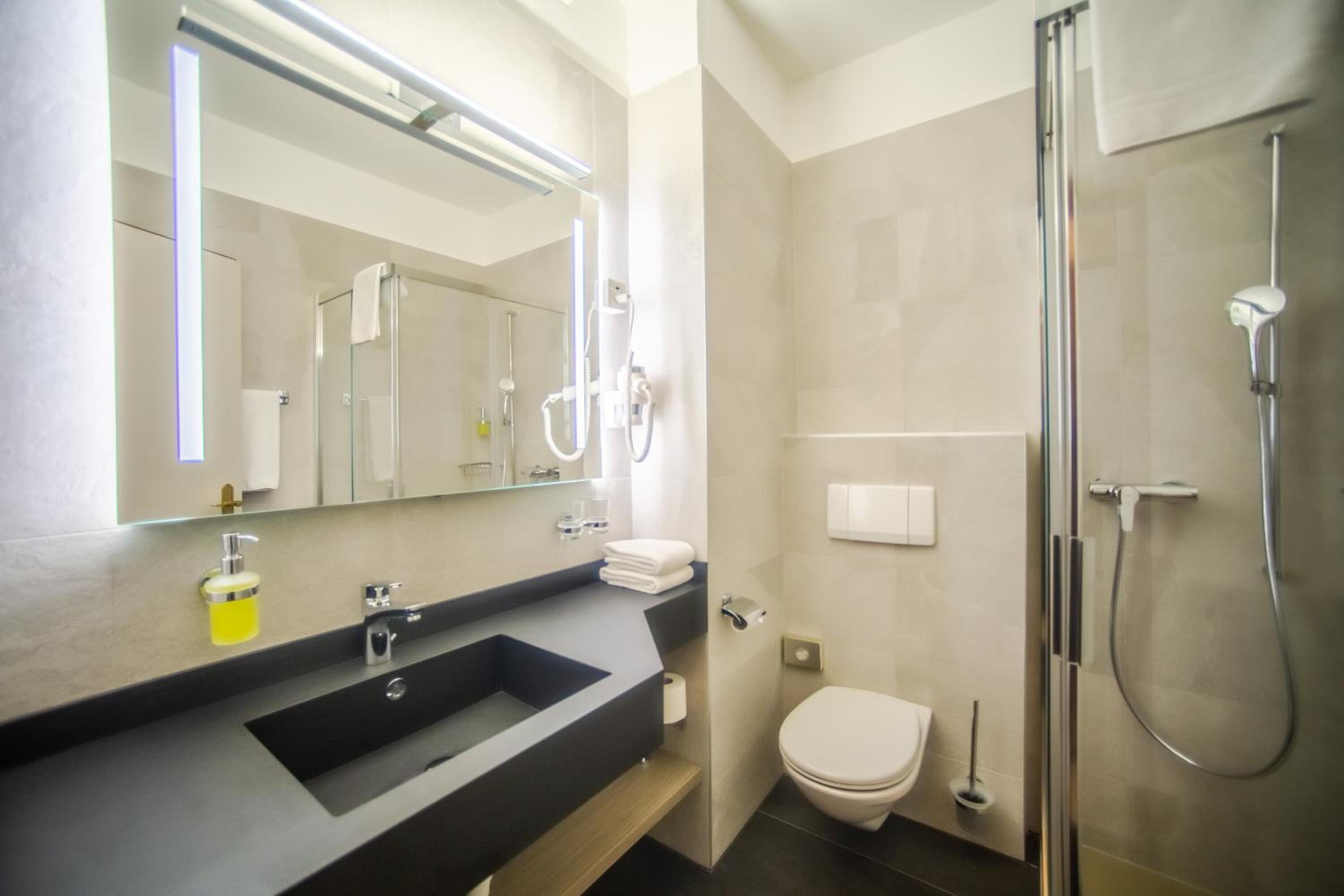A modern bathroom with a large mirror, a sink, a toilet, and a shower.