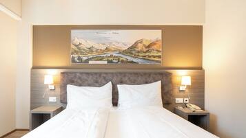 A hotel room with a large bed, two bedside tables, a headboard, and a wall-mounted painting of a landscape.