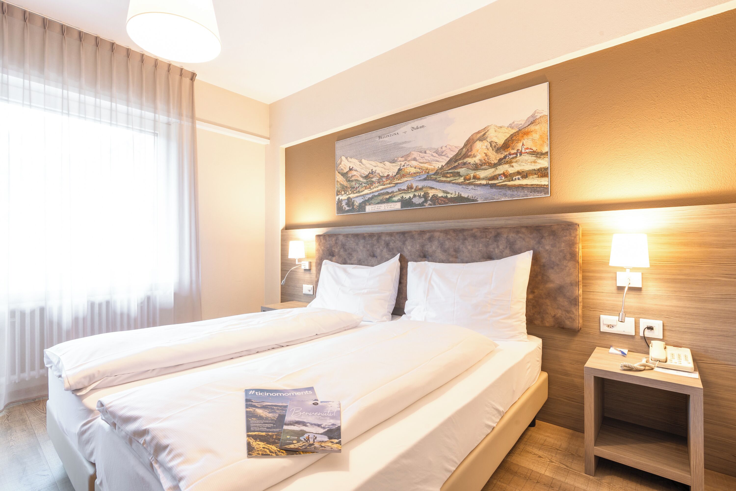Habitación de hotel con una cama grande, cabecera con pintura, lámparas de noche y mesita de noche con teléfono y control remoto.