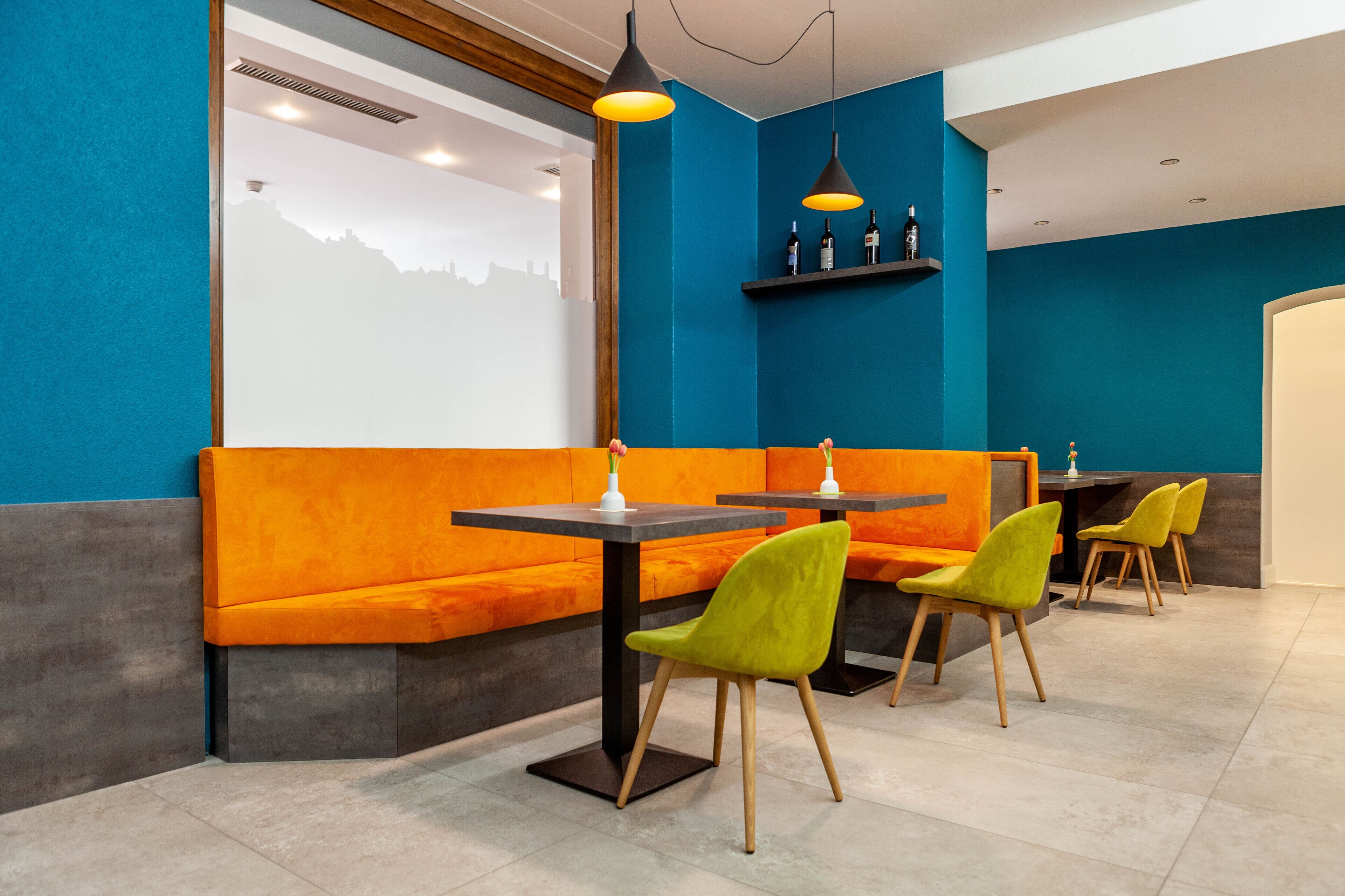 A modern restaurant interior with orange seating, green chairs, and black tables.