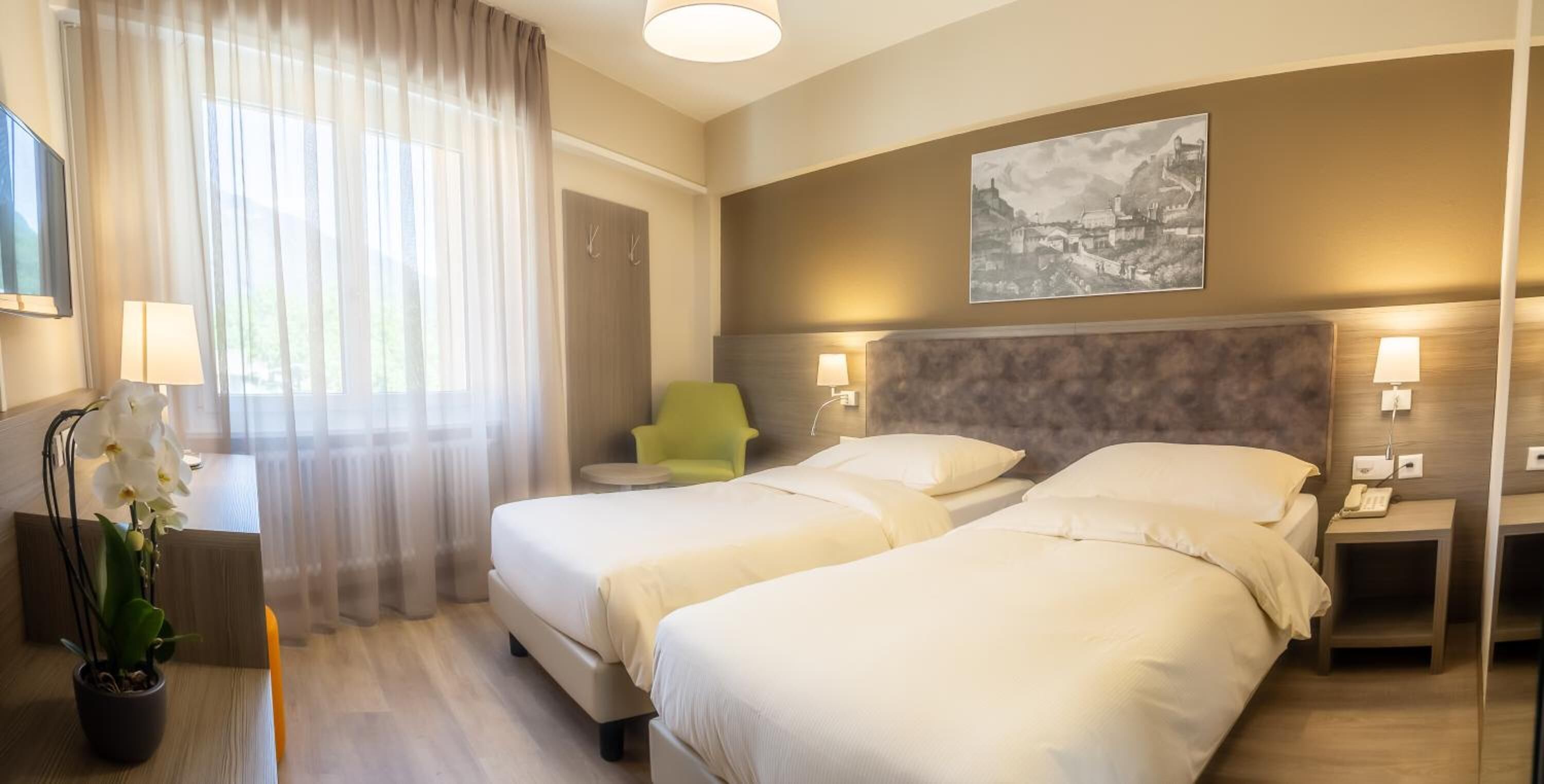 A hotel room with two beds, a desk, a chair, a potted plant, and a painting on the wall.
