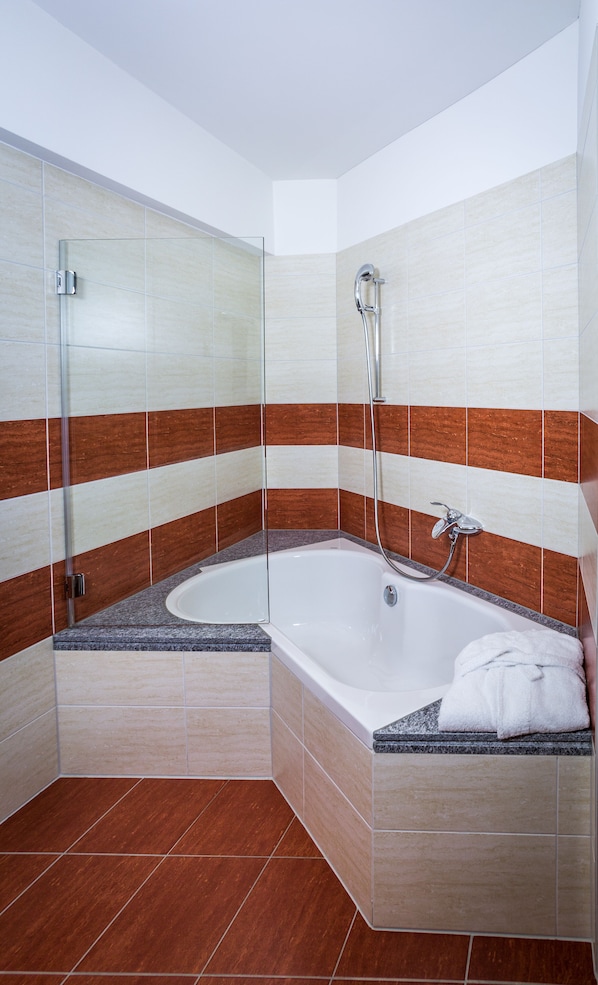 A corner bathroom with a freestanding bathtub, a glass shower enclosure, and a towel on the tub. - Hotel Unione (Bellinzona)
