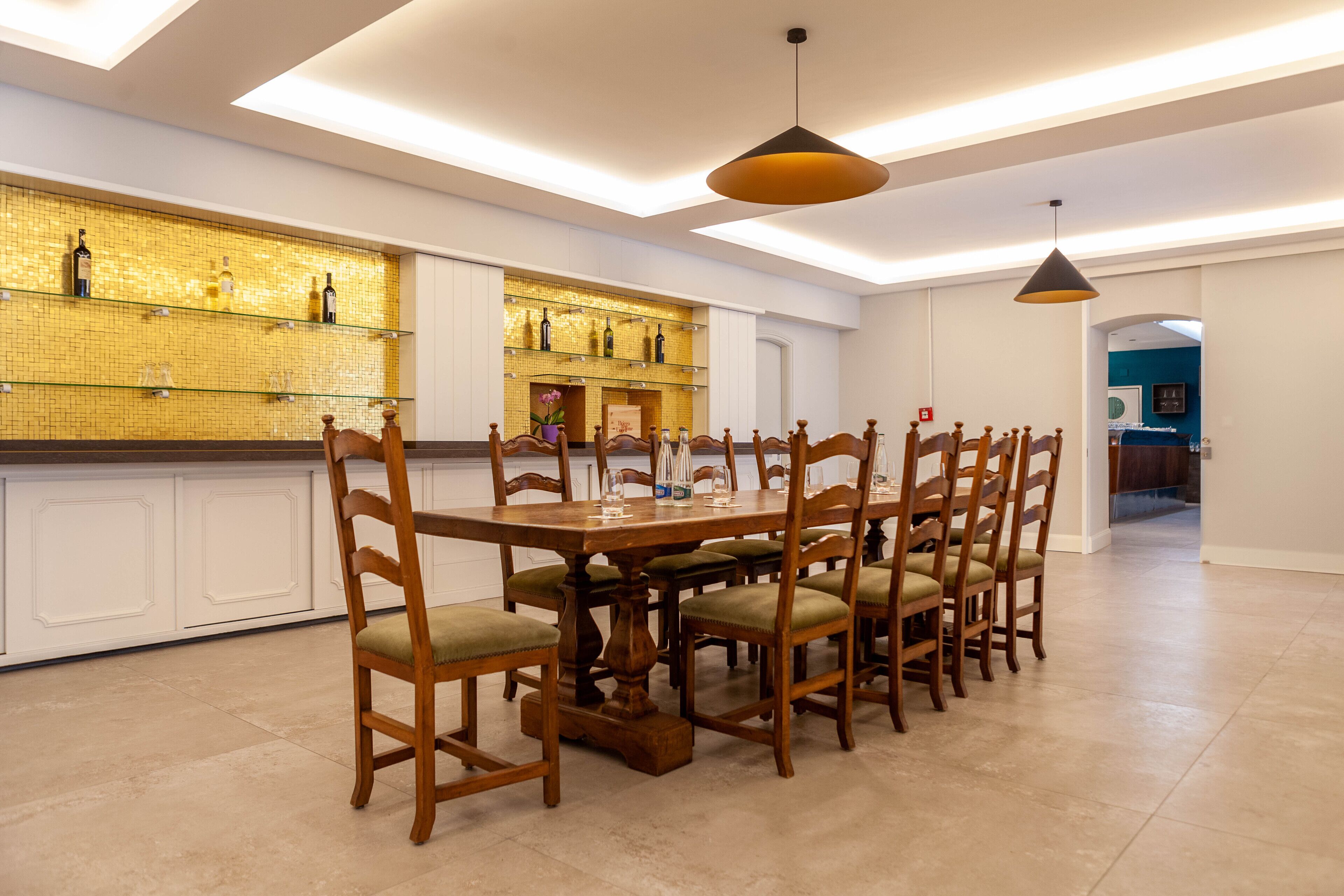 A spacious dining area with a long wooden table and matching chairs, a tiled backsplash with bottles, and pendant lighting.