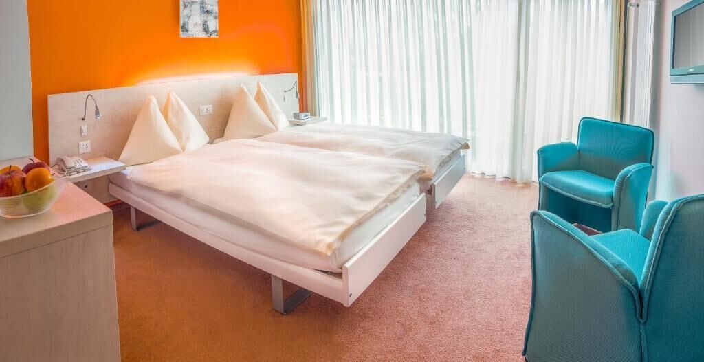 Habitación de hotel con dos camas, un escritorio con frutero, televisor y una silla azul.