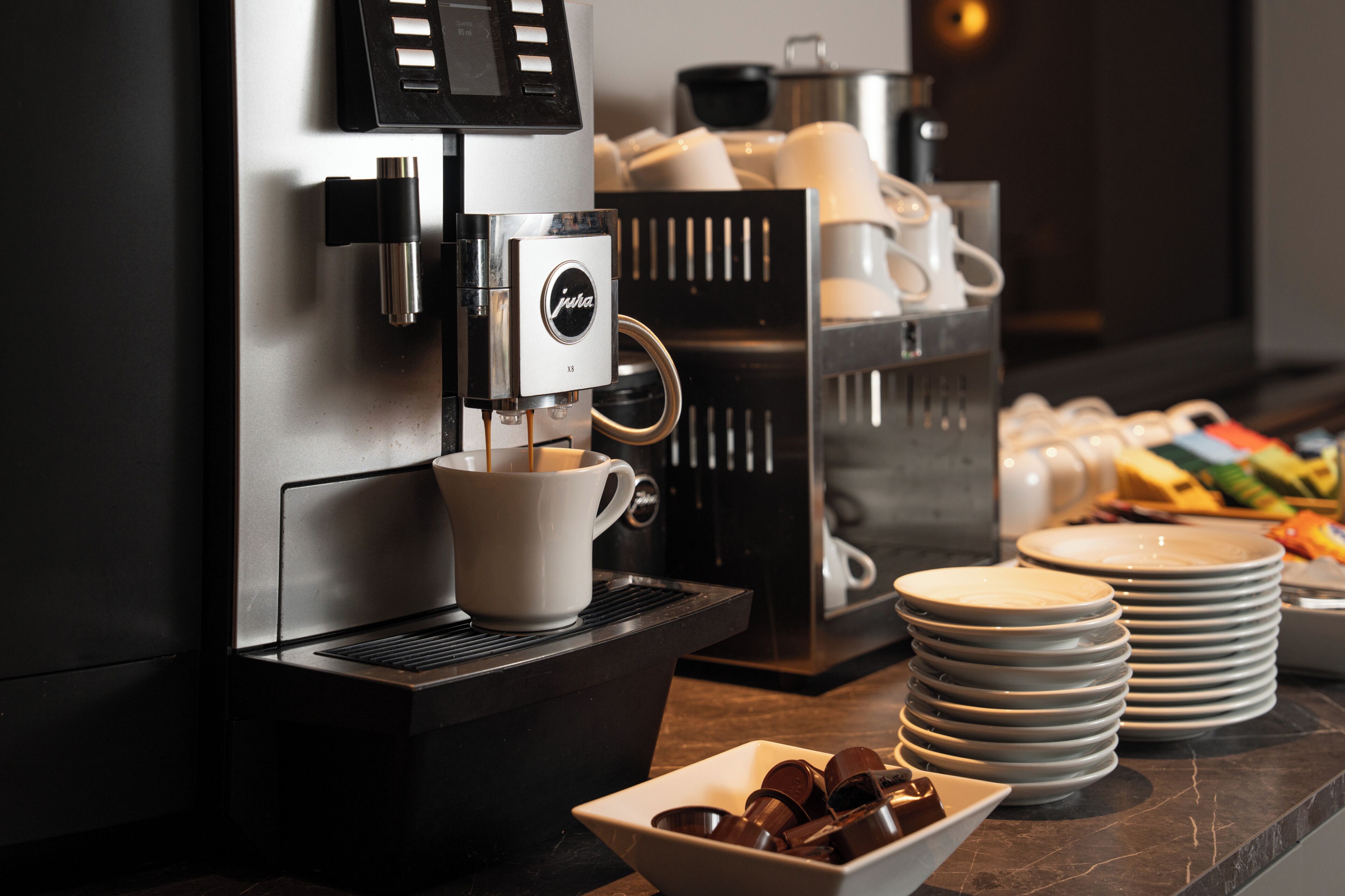 Eine Kaffeemaschine mit Tasse, gestapelten Tellern und einer Schale Schokoladenguglhupf.
