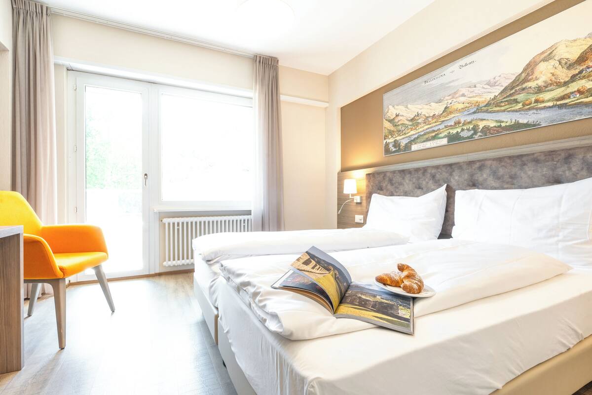 A hotel room with a large bed, a reading area with a chair, and a painting on the wall.