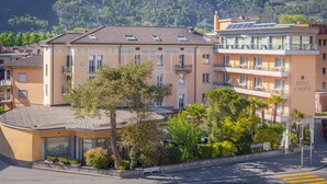 Un hotel de estilo arquitectónico tradicional, con un patio central con árboles y una fuente, varios balcones y vistas a un paisaje montañoso.