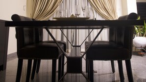 Uma sala de jantar com uma mesa e cadeiras, um lustre, cortinas e uma planta.